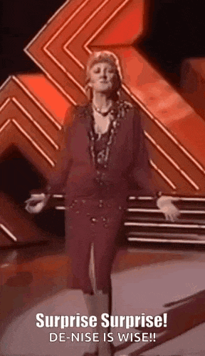 a woman is standing on a stage with her arms outstretched and a surprise surprise ! de-nise is wise !