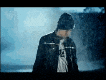 a man is standing in the rain wearing a hat and a jacket .