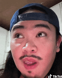 a man with long hair and a beard is wearing a blue hat and sticking his tongue out