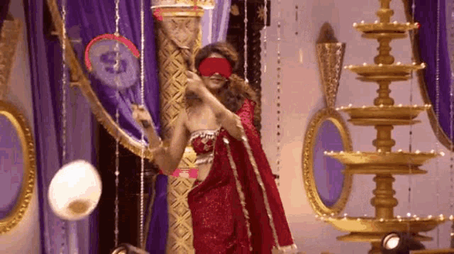 a woman in a red saree is wearing a blindfold and holding a badminton racket .