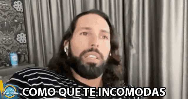 a man with long hair and a beard says " como que te incomodas " while wearing headphones