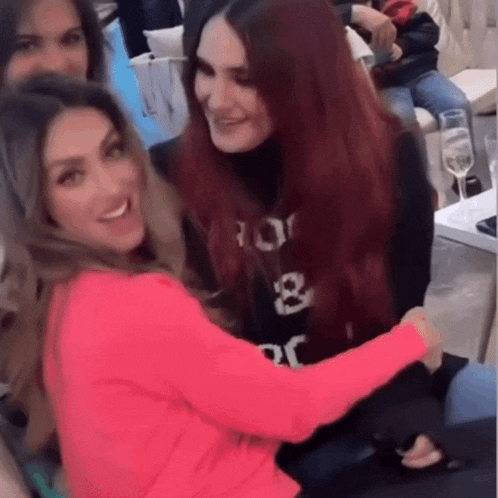 a woman in a pink sweater with the letters r on it is hugging another woman