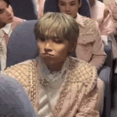 a man in a pink jacket is sitting in a crowd of people making a face .