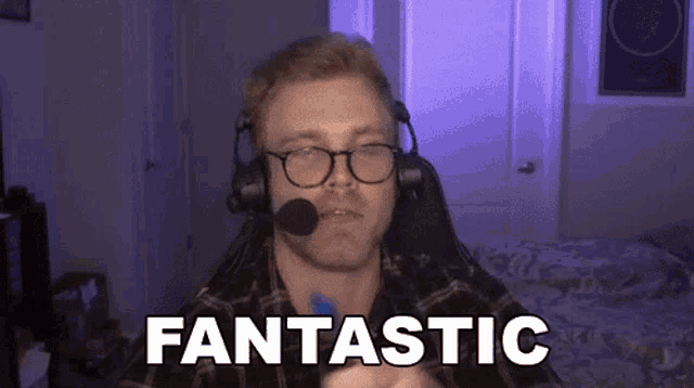 a man wearing headphones and glasses says fantastic in front of a bed