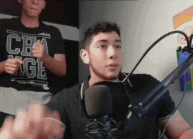 a man is giving a thumbs up while sitting in front of a microphone in a room .