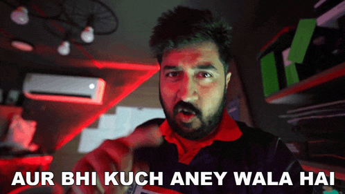 a man in a red shirt says " aur bhi kuch aney wala hai " in a dark room