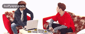 two young men are sitting on a couch talking to each other and one of them is using a laptop .