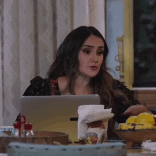 a woman is sitting at a table working on a laptop computer .