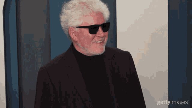a man wearing sunglasses and a black suit smiles for the camera