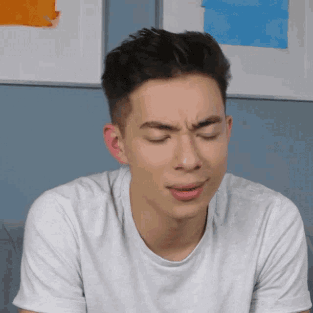 a young man in a white t-shirt is making a face with his eyes closed