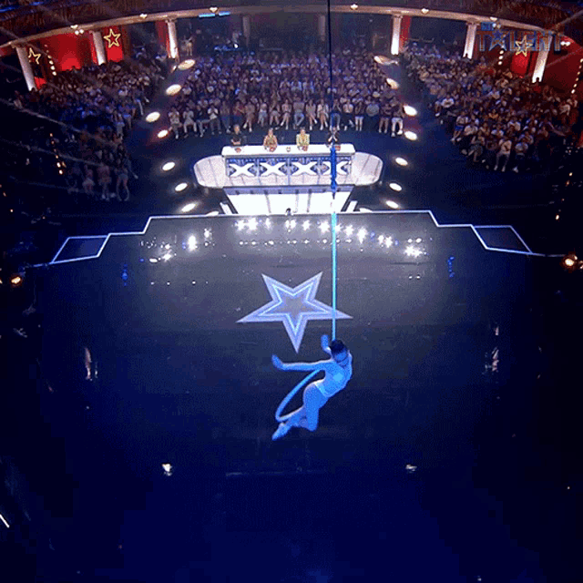 a person is hanging from a pole in front of a crowd that is watching a show called america 's got talent