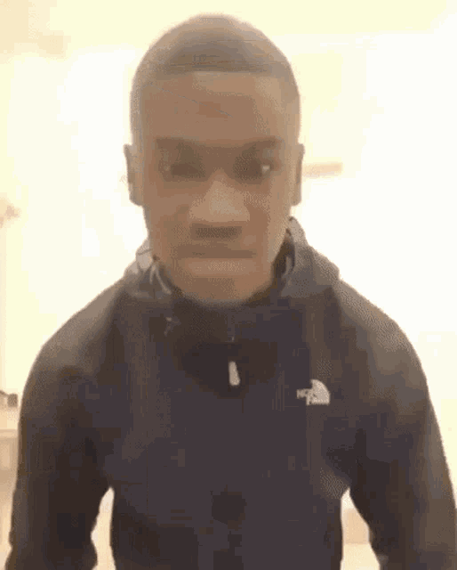 a young man wearing a black jacket with the north face logo on it is making a funny face .