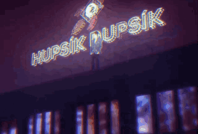 a man stands in front of a neon sign that reads hupsik