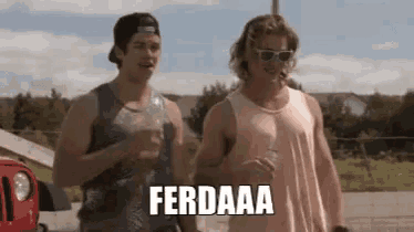 two men are standing next to each other and one of them is wearing sunglasses and a tank top .