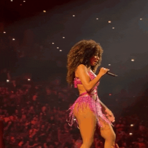 a woman in a pink outfit is dancing on stage in front of a crowd