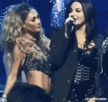 two women are singing into a microphone on a stage .