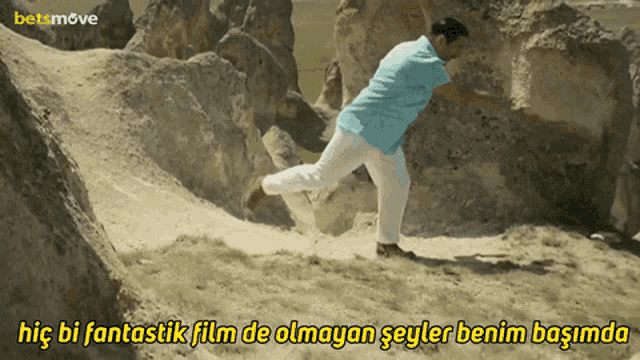 a man in a blue shirt and white pants is running on a rocky hillside with a betsmove logo behind him