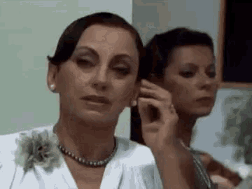 two women are standing next to each other in a room . one of the women is wearing earrings .
