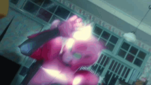 a pink cartoon character is standing in a room with a blurred background .