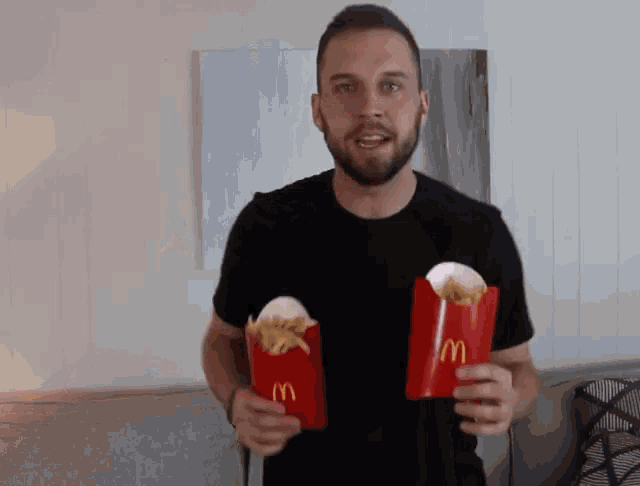 a man in a black shirt is holding two mcdonald 's french fries