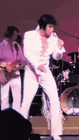 a man in a white suit is singing into a microphone on a stage