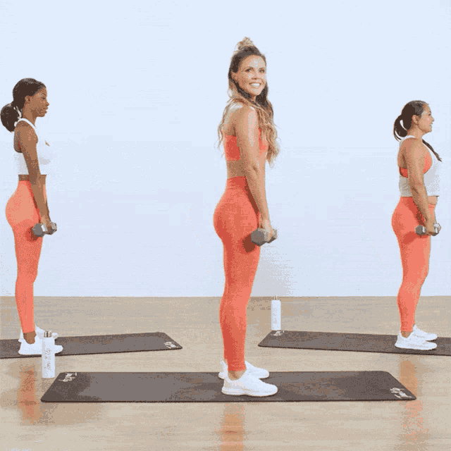 three women are standing on yoga mats holding dumbbells in their hands
