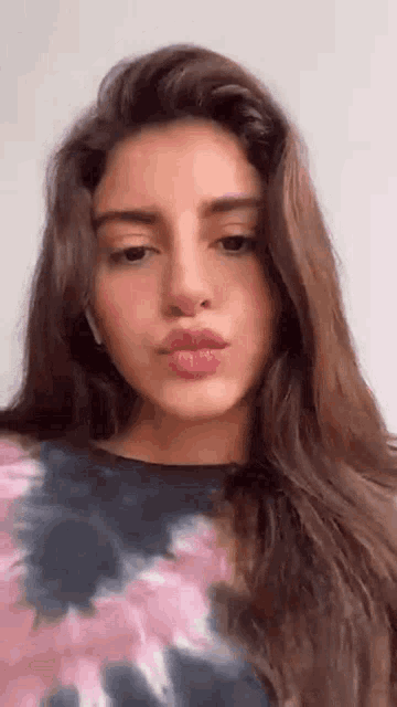 a close up of a woman 's face with long hair and a tie dye shirt .