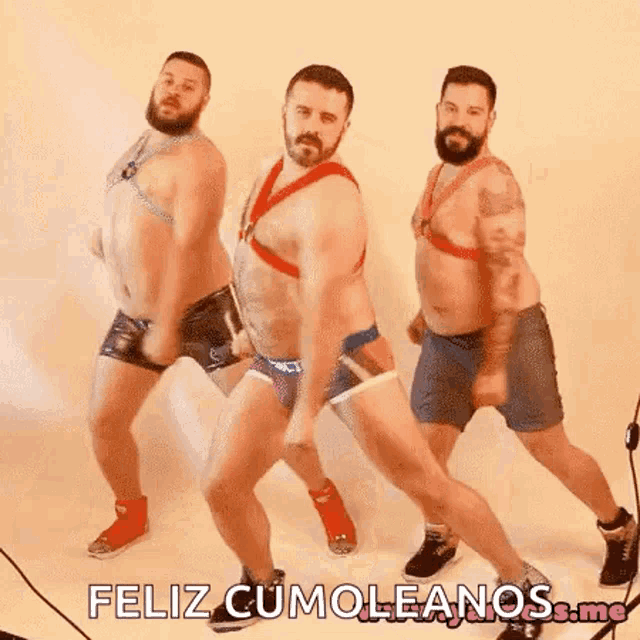 three men in underwear are dancing in front of a white wall and they are wearing harnesses .