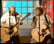two men playing guitars and singing into microphones in front of a sign that says cal