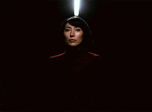 a woman in a red sweater is standing in the dark with a light shining on her face .