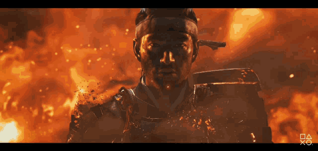a man in armor stands in front of a fire with a playstation logo in the lower right corner