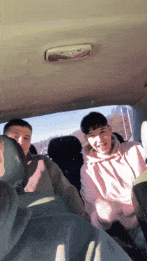 a man in a pink hoodie sits in the back seat of a car with other people