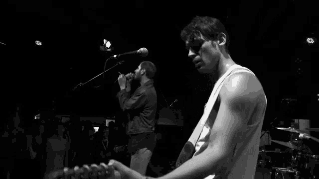 a man is singing into a microphone while another man plays a guitar on stage in a black and white photo .
