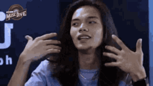 a young man with long hair is making a funny face while holding his hands to his head .