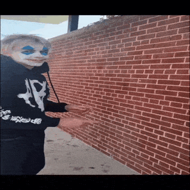 a person with a clown face painted on their face is pointing at a brick wall