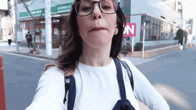 a woman wearing glasses and a backpack stands in front of a pink sign that says no parking
