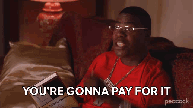 a man is sitting on a couch holding a book and says you 're gonna pay for it