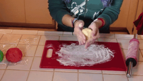 a woman is kneading dough on a cutting board with a rolling pin