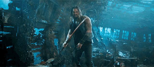 a man with long hair and a beard is standing in the water holding a stick