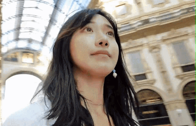 a woman with long black hair stands in front of a building with arches