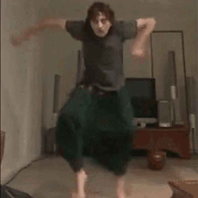 a man is jumping in the air in a living room while wearing green pants .