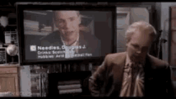 a man in a suit and tie is standing in front of a television screen that says needles on it .