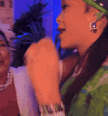 a woman wearing a bandana and earrings is singing into a microphone while standing next to another woman .