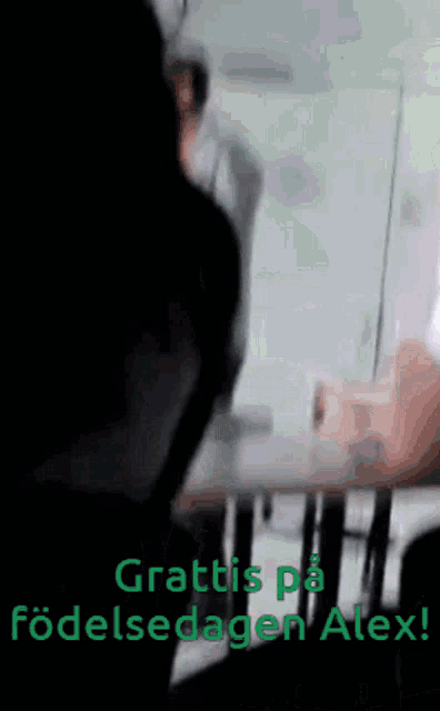 a blurred image of a person sitting at a table with the words grattis pa fodelsdagen alex