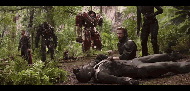 a man in a black suit is laying on the ground surrounded by a group of people