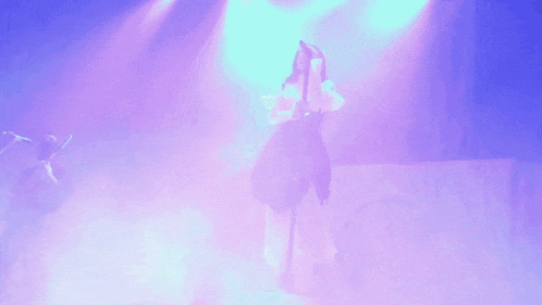 a woman is singing into a microphone while standing on a stage with purple lights behind her