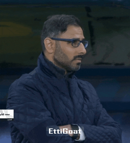 a man wearing glasses and a blue jacket says " ettigoat " on the bottom right