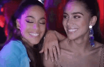 two women are smiling and hugging each other in a club .