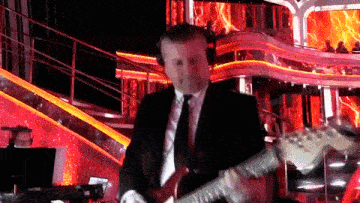 a man in a suit and tie is playing a red guitar