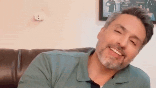 a man with a beard is sitting on a couch smiling with his eyes closed .